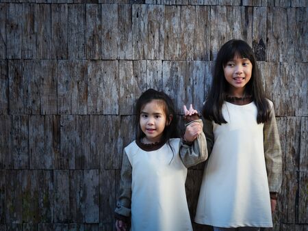 The 2 sisters standing on the wood wall and older sister catch the hand of her sister with smilingの写真素材