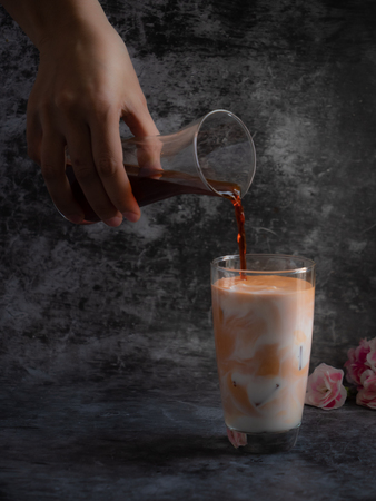 Hand hold the glass of tea puring to mix in the milk with dark backgroundの写真素材