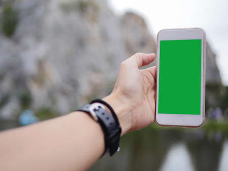 Mobile phone in the hand with green colour screen to show at the mountain backgroundの写真素材
