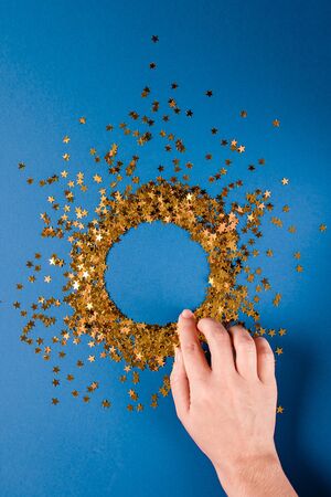 A circle of golden confetti sparkles in female hands on a dark blue background. Christmas concept. Birthday. Background.の写真素材
