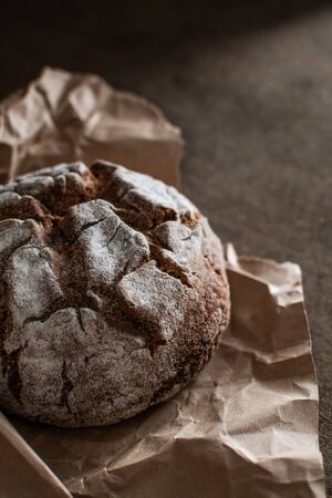 Freshly baked rye bread in craft paper on a dark brown background. Vertical frame. Handicraft...