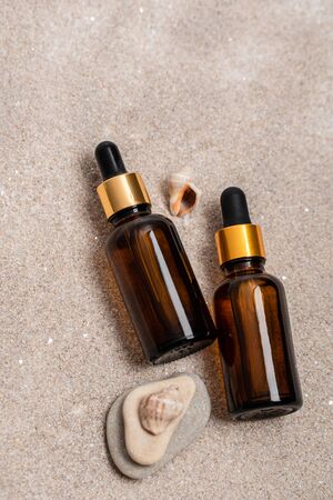 Glass brown bottles of serum with a pipette for skin care is on the sand with stones and shells. Cosmetics with marine components. The concept of health and beauty. minimalism, copy spaceの写真素材