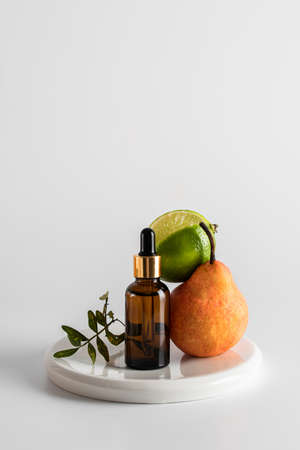 Glass brown bottle with serum and a pipette for skin care on a light background. composition with lime, pear and olive branch. The concept of health and beauty. minimalism, copy spaceの写真素材