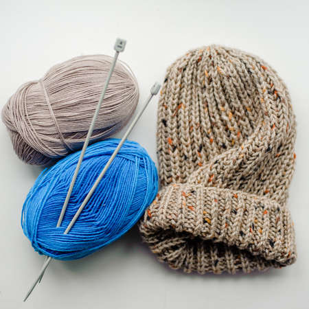 Blue and beige knitted wool skeins and a knitted hat on a light background. Alpaca, merino yarn....