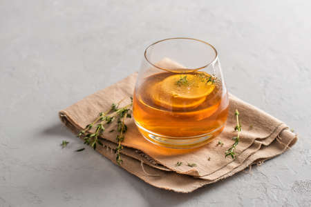 Hot tea in a glass with lemon and thyme on a linen napkin, gray background with copy space. Autumn...