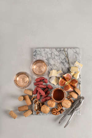 Brie and cheese with paprika, salami, figs, walnuts, honey and rose wine on a marble board. Food for a romantic date on a light concrete background. Top viewの写真素材