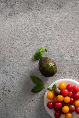 Fresh cherry tomatoes on a plate, avacado and basil leaves on a gray background. Vegetarianism.の写真素材