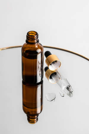 A glass brown serum bottle with a skin care dropper stands on the mirror. Reflections. Health and...