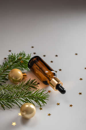 Christmas minimalistic composition with brown glass bottle of serum on the background of the Christmas tree and golden balls. Health and beauty concept. Copy spaceの写真素材