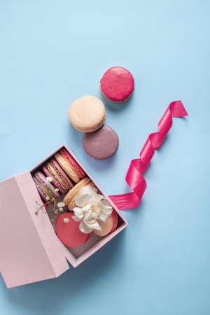 Beautiful composition with multi-colored macarons, flowers and a pink ribbon on a blue background. French cuisine,の写真素材
