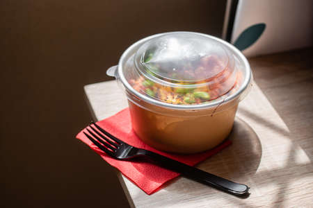 Healthy poke bowl dish with salmon and vegetables in kraft paper packaging on a wooden table. Takeout food. Fitness food. Dinner. Nutrition conceptの写真素材