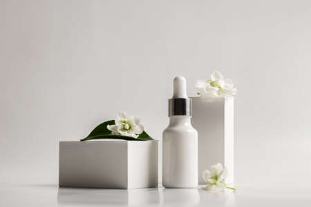 Composition of a white glass dropper bottle with a skin care product and white flowers on a white background. Health and beauty conceptの写真素材