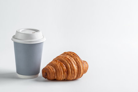 Hot drink in a craft glass and a lush delicious croissant on a white backgroundの写真素材