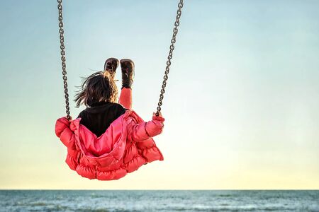 Little girl on the swing watching the sunset over the seaの写真素材