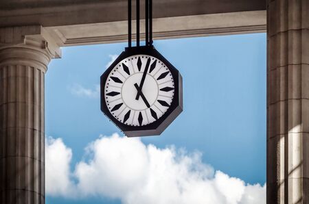 The clock of the Central Station in Milan, Italy, stands between the columns of the porch in front of the lobby. In the background a blue sky with a few passing clouds.の写真素材
