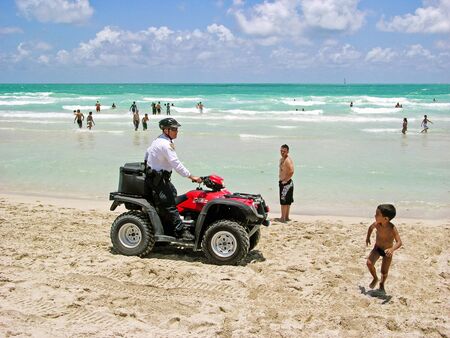 Miami, Florida, USA - May 28, 2007: A policeman on patrol, riding his quad-bike red, runs the beach attracting the looks of some bathers, while a child runs away scared.のeditorial素材