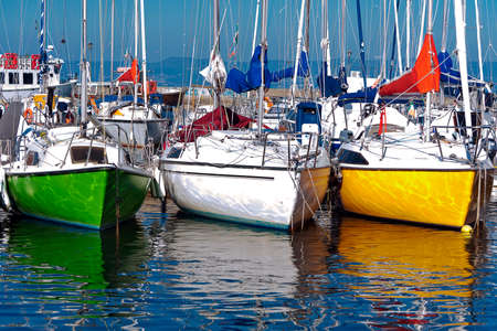 Colored sail boats parked on the dock of a lake. Yellow, green, white, color reflections on water.の写真素材