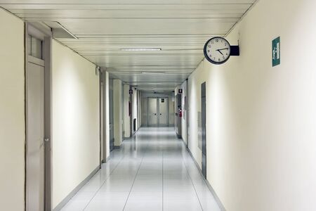 Long hospital corridor, with side doors and a wall clock. At the bottom of a door marks the entrance to another area.の写真素材