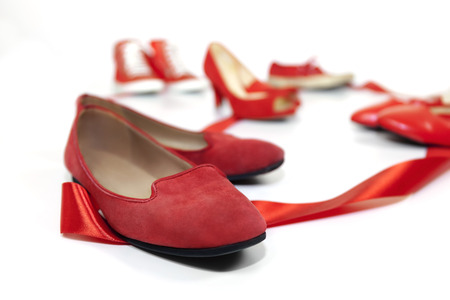 Red shoes women of various models, are based on a white floor and are joined by a red ribbon, which is the common thread that unites them: violence against women, symbolized by red shoes.の写真素材