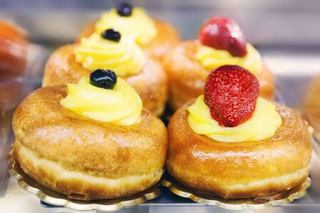 Two baba, one with yellow cream and black cherry, the other with yellow cream and strawberry.の写真素材