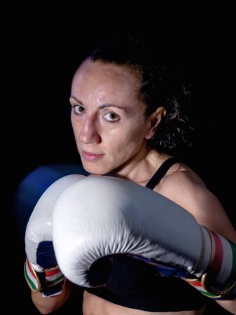 Boxer woman with boxing gloves. Portrait with half bust on black background, artificial lighting.の写真素材