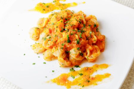Ready dish of pasta topped with pumpkin, tomato, oil and parsley. White plate on a white background. Italian cuisine.の写真素材