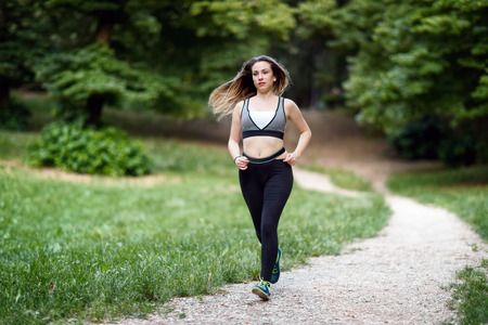 A young woman runs along a path in the green of the natural park. Daylight, summer, among the trees of a public garden.の写真素材