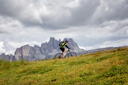 Cortina d'Ampezzo, Italy - August 18, 2018: a solo cyclist pedal uphill on the mountain path, on a cloudy summer day. In the background, the peaks of the dolomites (Croda da Lago).のeditorial素材