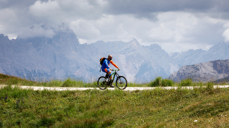 Cortina d'Ampezzo, Italy - August 18, 2018: a solo cyclist rides on the mountain path on a cloudy summer day. In the background, the peaks of the dolomites.のeditorial素材