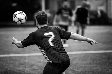 Rome, Italy - May 19, 2019: Football player in the soccer field chases the ball in a game action. A man, black shirt and shorts, framed from behind in the green soccer field.のeditorial素材
