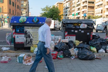 Rome, Italy - June 27, 2019: Garbage bins full of rubbish, among the streets and buildings of the city. A citizen looks at them in disbelief.のeditorial素材