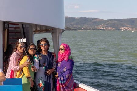 Castiglione del Lago (PG), Italy - July 14, 2019: A group of Indian women, with very colorful clothes, take a selfie from the boat that will take them on a visit to the Isola Maggiore on Lake Ttrasimeno.のeditorial素材