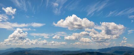 Landscape from the top of the mountains. The horizon between heaven and earth is composed of mountain peaks and a cloudy blue sky. A summer day with sunlight.の写真素材