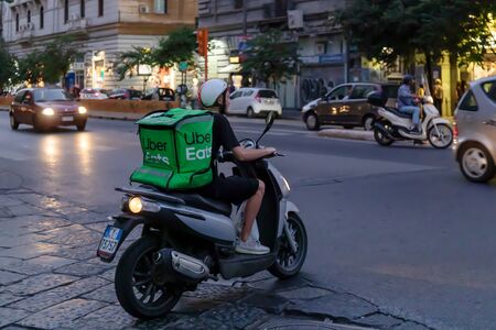 Naples, Italy - August 10, 2019: Uber Eats, a boy with a scooter with the typical green backpack,...
