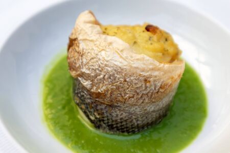 Sea bass with pea sauce, served in a white plate. Italian restaurant menu. Sea bass cooked in the oven and prepared in a spiral on a puree of green peas.の写真素材
