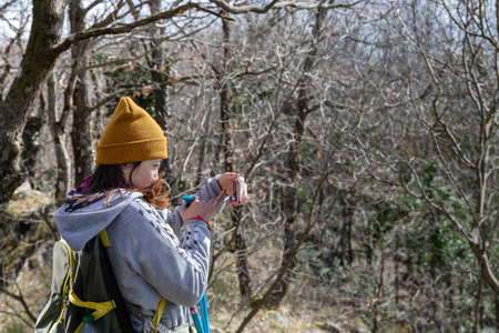 Rocca di Papa, Italy - February 29, 2020: Girl of Asian origin photographing the woods with her cell phone during a hike in the mountains.のeditorial素材