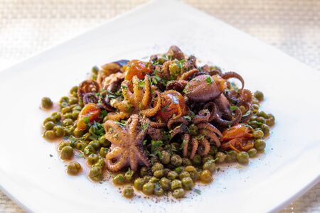 Small octopuses cooked with cherry tomatoes, oil and peas. Tasty dish of Italian cuisine served on...