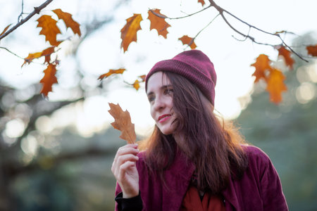 In the autumn season a girl strokes a dry leaf in the public park surrounded by autumn foliage.の写真素材