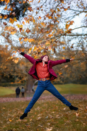 A girl in winter clothes, jeans and a hat, jumps for joy in the foliage of the autumn forest.