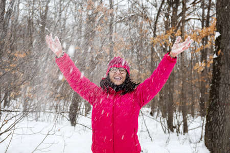 In the snowy forest, a woman dressed in mountain clothes, a pink down jacket, gloves and a wool hat,...