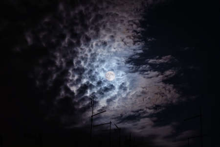 Full moon at night. The illuminated face of the moon is wrapped in a cloud cover that covers it in a veiled way.の写真素材