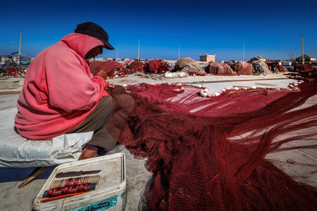 Essaouira, Morocco - August 2, 2023: Picturesque fishing port on the Atlantic coast of Morocco, a man mends fishing nets on the quay.のeditorial素材