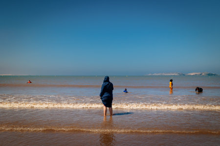 Essaouira, Morocco - August 3, 2023: A woman in traditional clothing and a headdress watches the sea from the beach. The Muslim religion prevents women from showing their bare bodies on mixed beaches.のeditorial素材