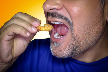Close-up of a hungry man biting into a prawn. Irresistible craving for food. Yellow background.の写真素材