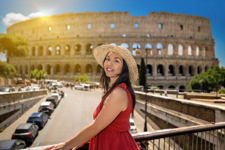 Girl in a straw hat and a red dress admires the ancient Colosseum in Rome in Italy. The tourist visits the most famous monument of ancient Rome.の写真素材