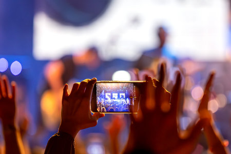 The audience records videos and takes photos with their smartphones during the concert of the musical band that performs on stage.の写真素材
