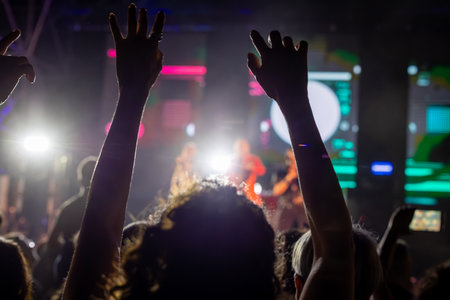 The audience gets excited and cheers with their arms raised during the concert of the musical band that performs on stage.の写真素材