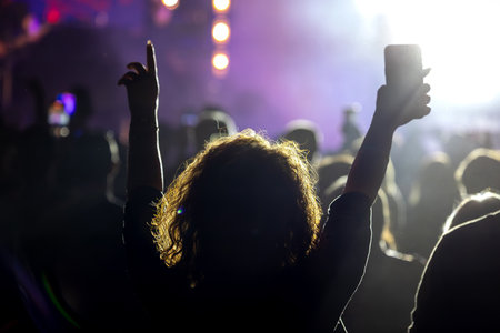 The audience gets excited and cheers with their arms raised during the concert of the musical band that performs on stage.の写真素材