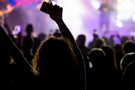 The audience gets excited and cheers with their arms raised during the concert of the musical band that performs on stage.の写真素材