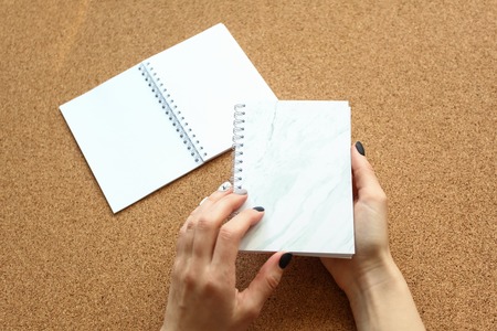 graceful hands of the girl with a closed notebook on the spring on the background of an open notepad on the corkwoodの写真素材